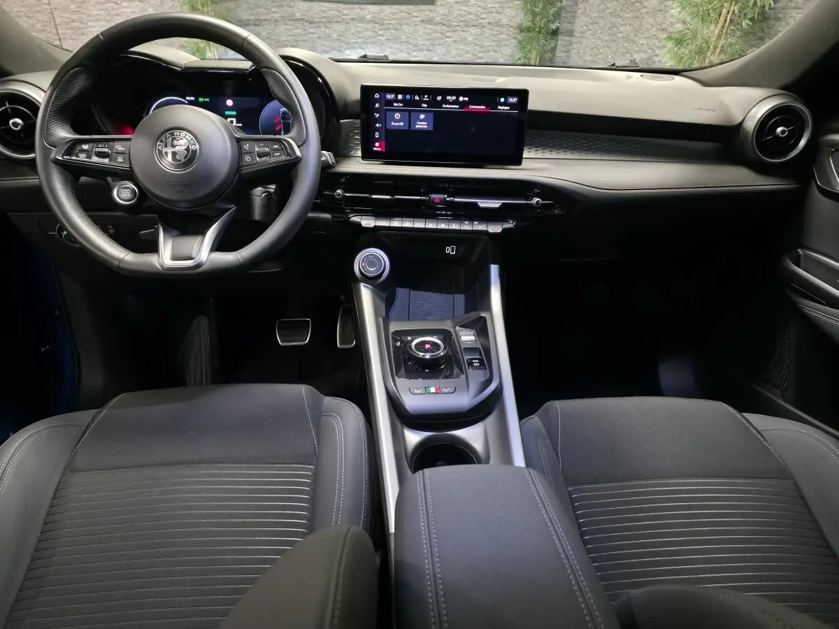 Vue intérieure avant de l'Alfa Romeo Tonale 2025, tableau de bord noir avec écran tactile et volant sport cuir.