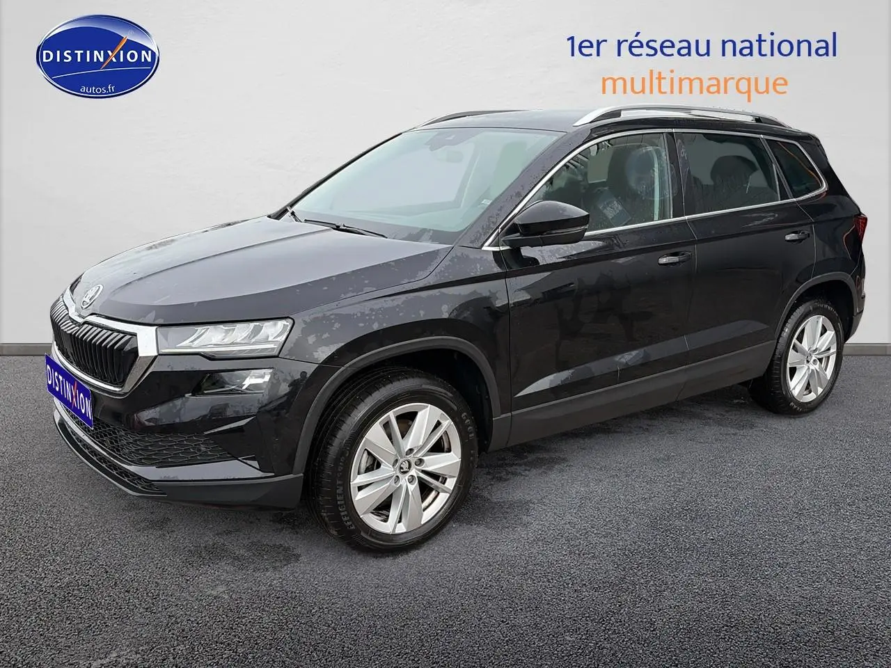 Vue 3/4 avant d’un Skoda Karoq noir 2025 avec jantes alu et barres de toit visibles sur fond neutre.