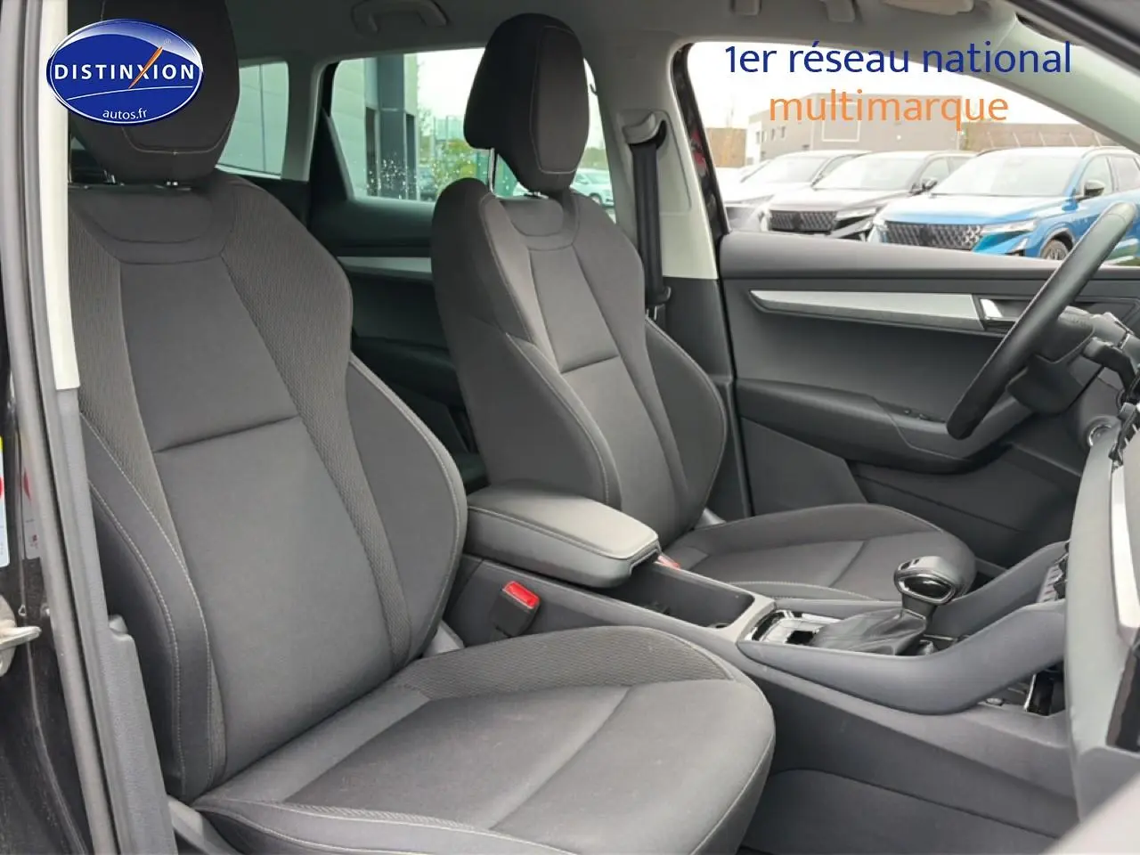 Intérieur avant du Skoda Karoq noir 2025, vue côté droit montrant sièges tissu gris et console centrale avec accoudoir.