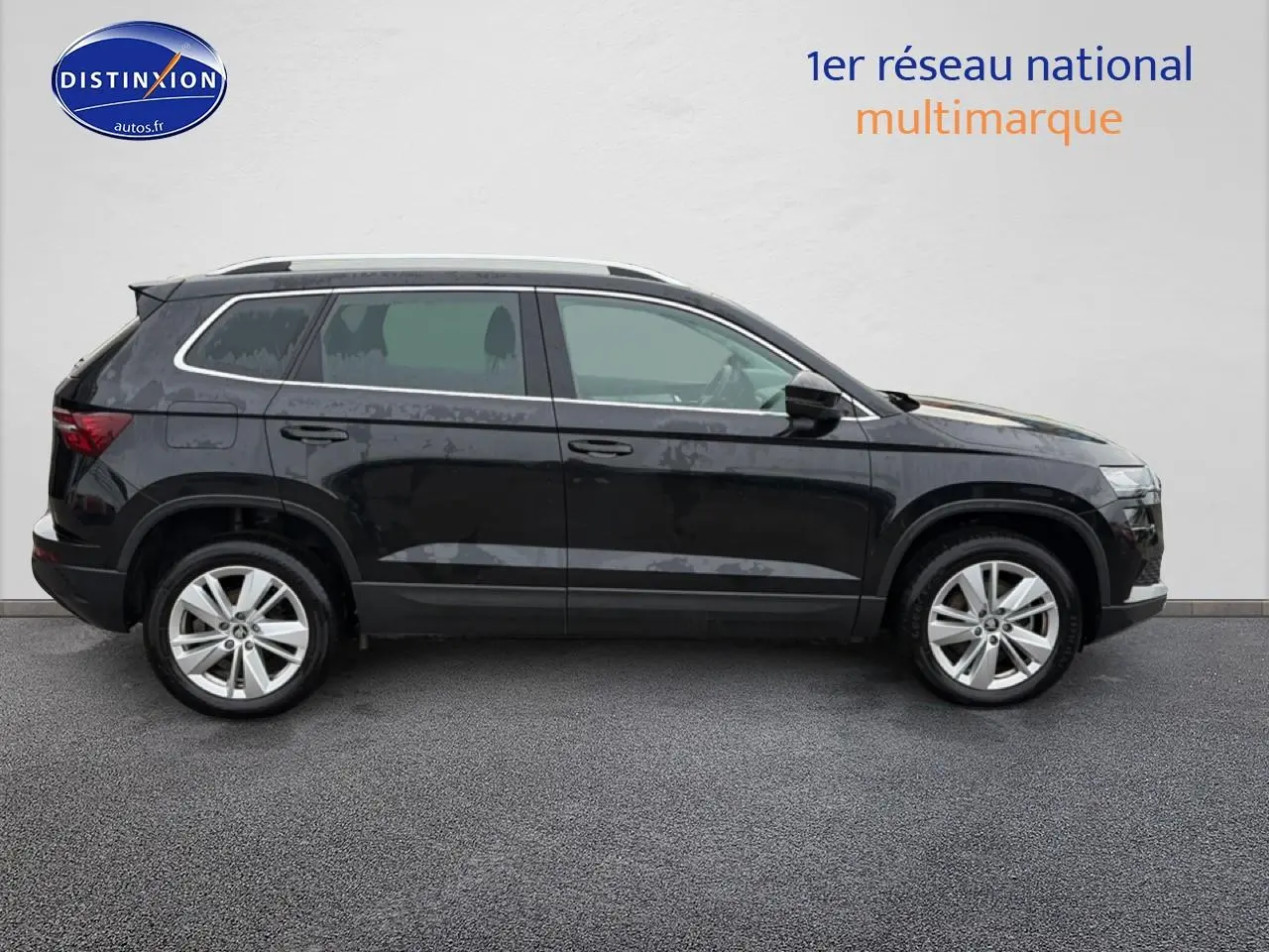 Profil droit d'un SUV Škoda Karoq noir 2025 avec jantes alu et barres de toit argentées sur fond neutre.