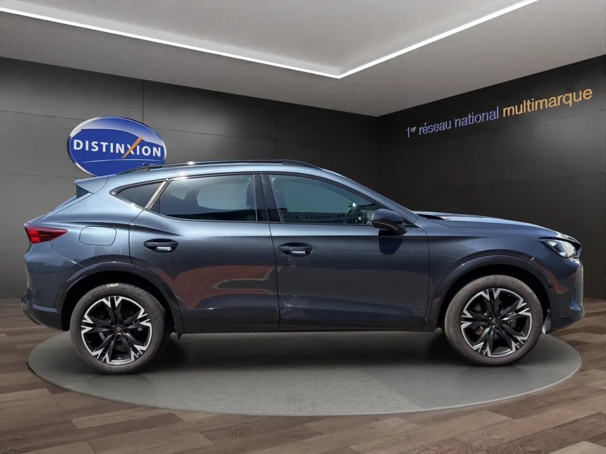 Profil droit du CUPRA Formentor gris foncé 2025 avec jantes alliage noires et toit ouvrant visible en intérieur showroom.