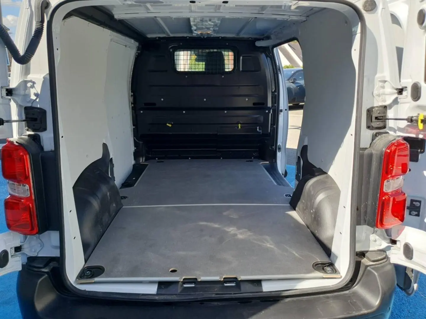 Vue arrière ouverte du Toyota Proace Fourgon blanc Glacier 2025, montrant l'espace de chargement avec plancher bois et cloison pleine noire.