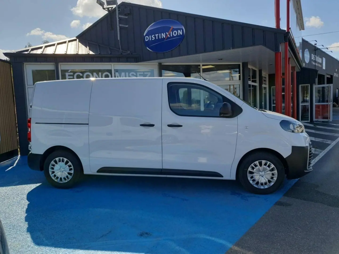 Vue de profil côté droit du Toyota Proace Fourgon blanc Glacier garé devant un bâtiment commercial.