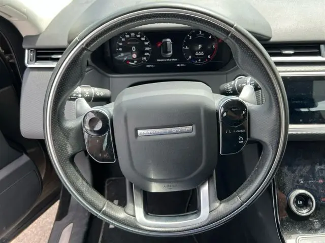 Vue rapprochée du volant noir du Range Rover Velar 2018 avec commandes intégrées et tableau de bord numérique.