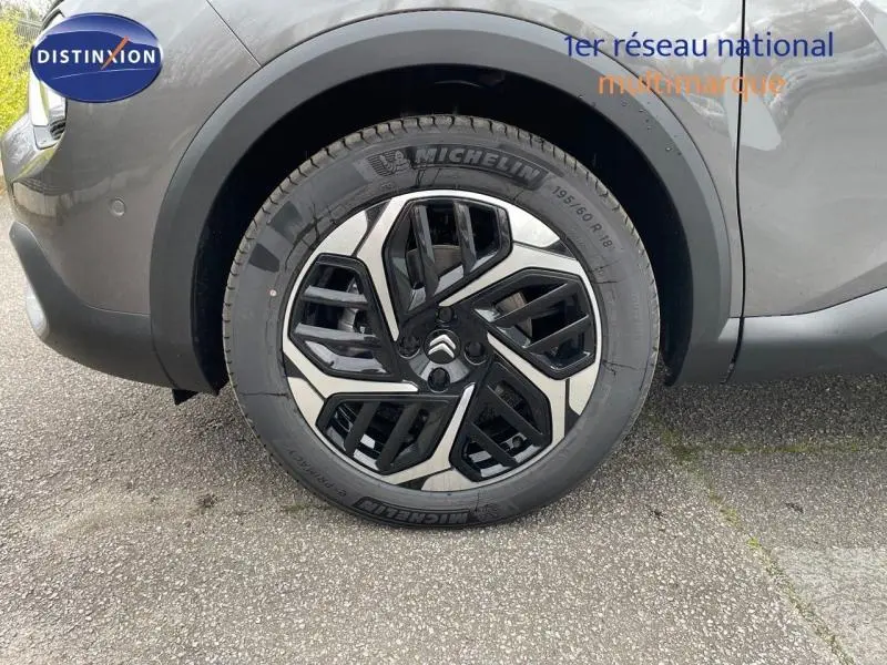 Gros plan sur la roue avant gauche gris métallisé d'une Citroën C4 1.2 Hybride 136ch avec jante alu au design géométrique noir et argent.