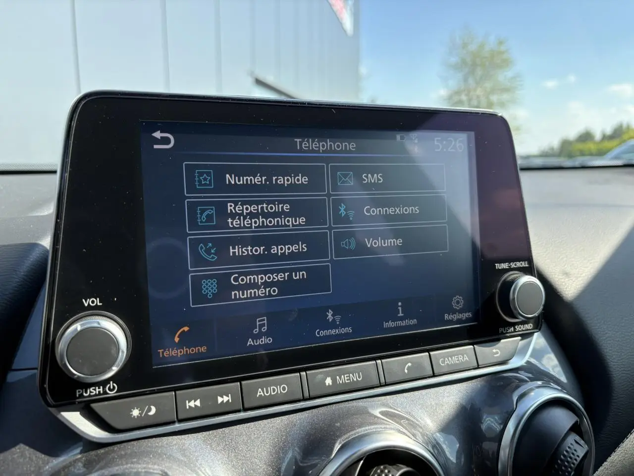 Écran tactile central du Nissan Juke gris Dark Metal 2024 affichant le menu téléphone avec commandes audio et caméra.
