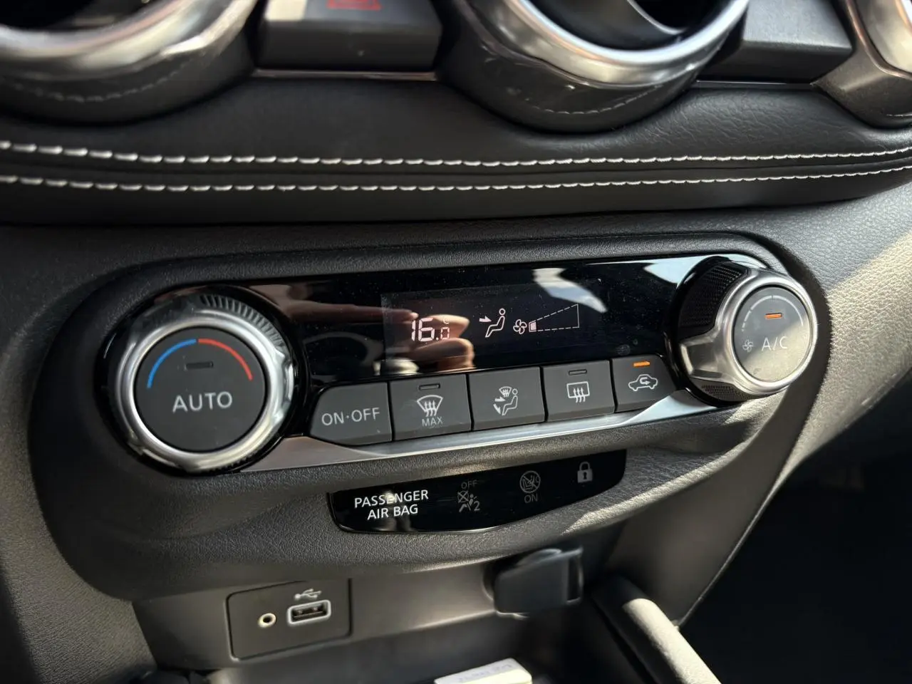 Vue rapprochée de la console centrale du Nissan Juke 2024 gris, montrant les commandes de climatisation automatique et port USB.