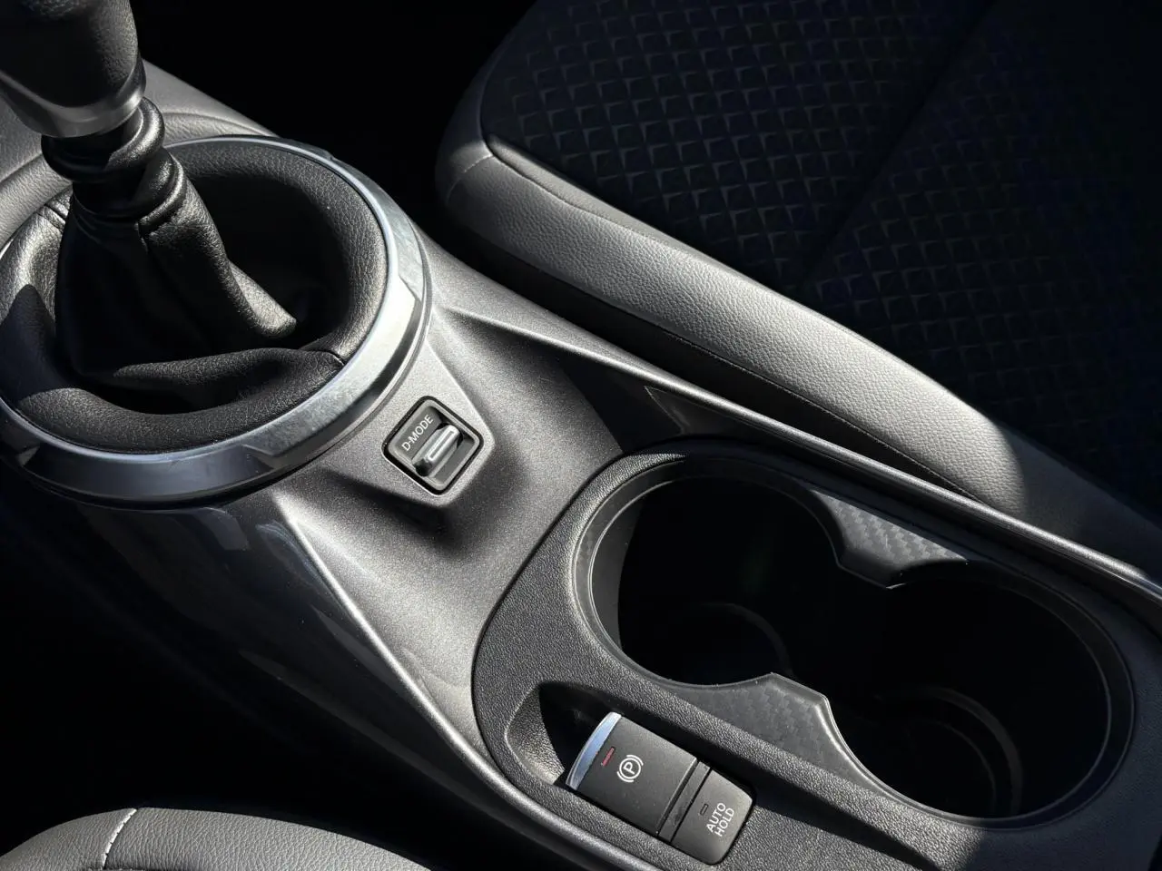 Gros plan sur la console centrale du Nissan Juke 2024 avec levier de vitesses manuel et bouton frein à main électrique.