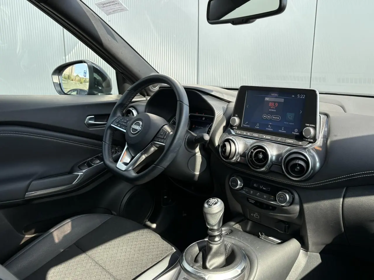 Intérieur du Nissan Juke 2024 vu côté conducteur, volant multifonction, écran tactile et levier de vitesse manuel visibles.