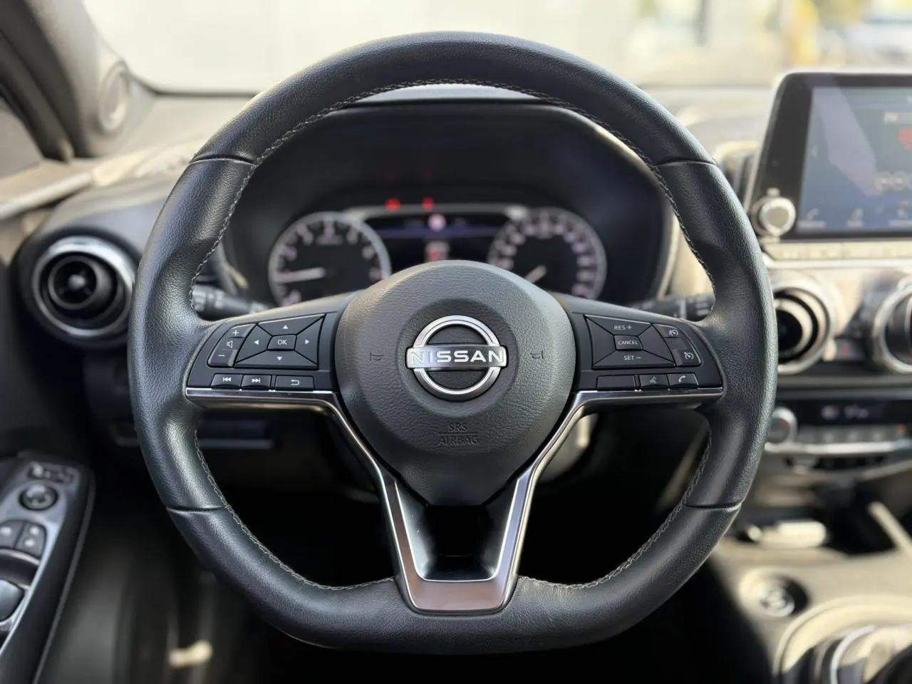 Volant en cuir noir de Nissan Juke 2024 avec commandes intégrées, tableau de bord et écran tactile en arrière-plan flou.
