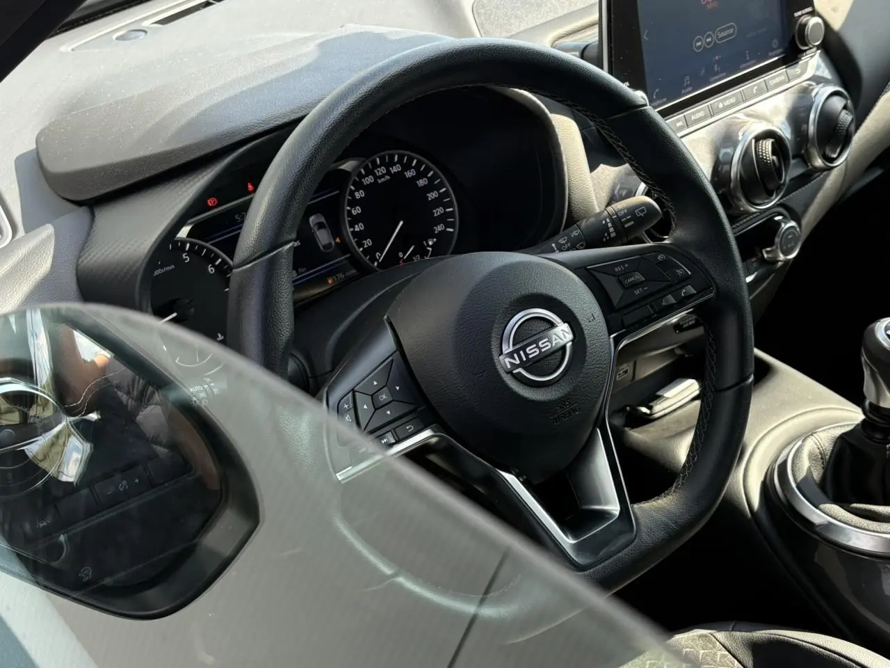 Vue rapprochée du volant noir et du tableau de bord du Nissan Juke 2024, avec levier de vitesses manuel visible.