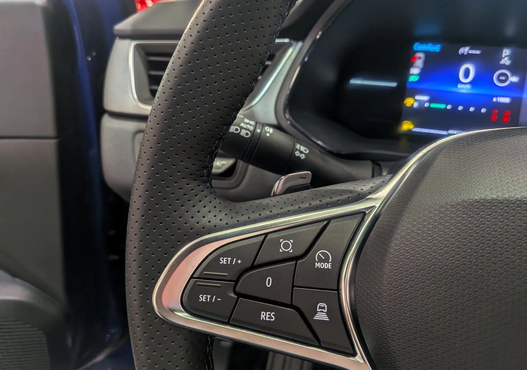 Gros plan sur le volant perforé du Renault Captur 2025 bleu Iron, avec commandes intégrées et tableau de bord numérique visible.