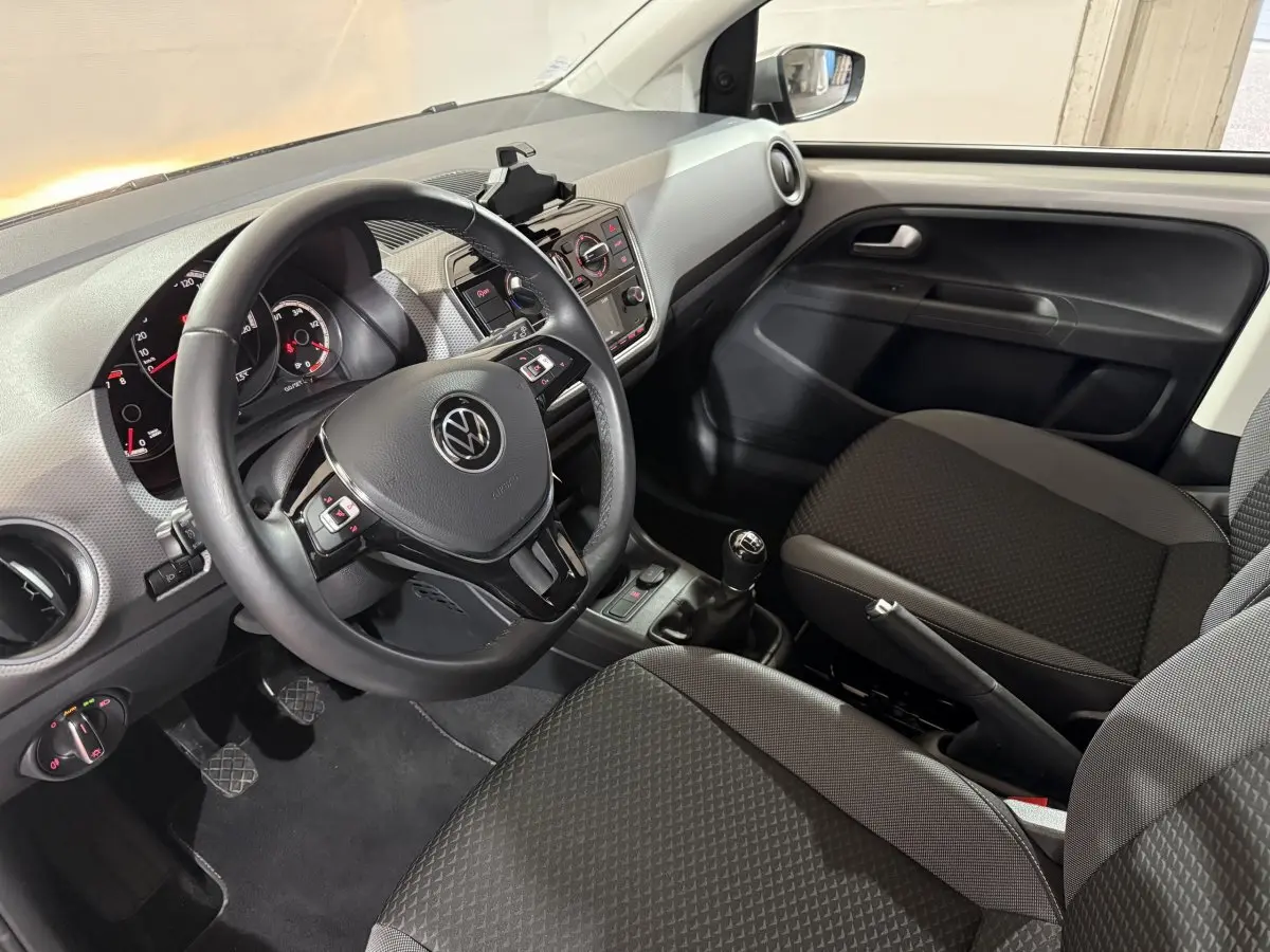 Vue intérieure côté conducteur de la Volkswagen Up 1.0 65 Active 2022, volant cuir et sièges tissu gris foncé.