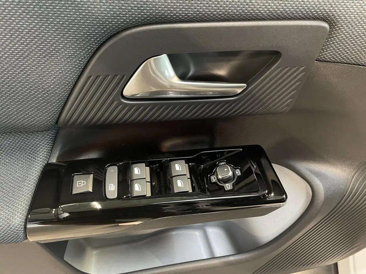 Gros plan sur la commande des vitres et rétroviseurs côté conducteur du Citroën C5 Aircross avec garniture noire texturée.