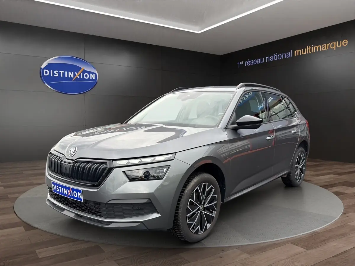 Skoda Kamiq gris foncé en 3/4 avant droit avec jantes bi-ton et calandre noire brillante dans showroom.