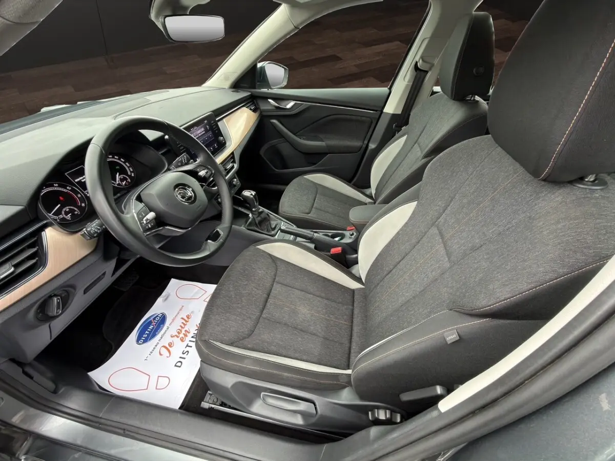 Vue intérieure côté conducteur du Skoda Kamiq 2023 gris foncé, mettant en valeur les sièges tissu bicolores et le tableau de bord avec écran tactile.