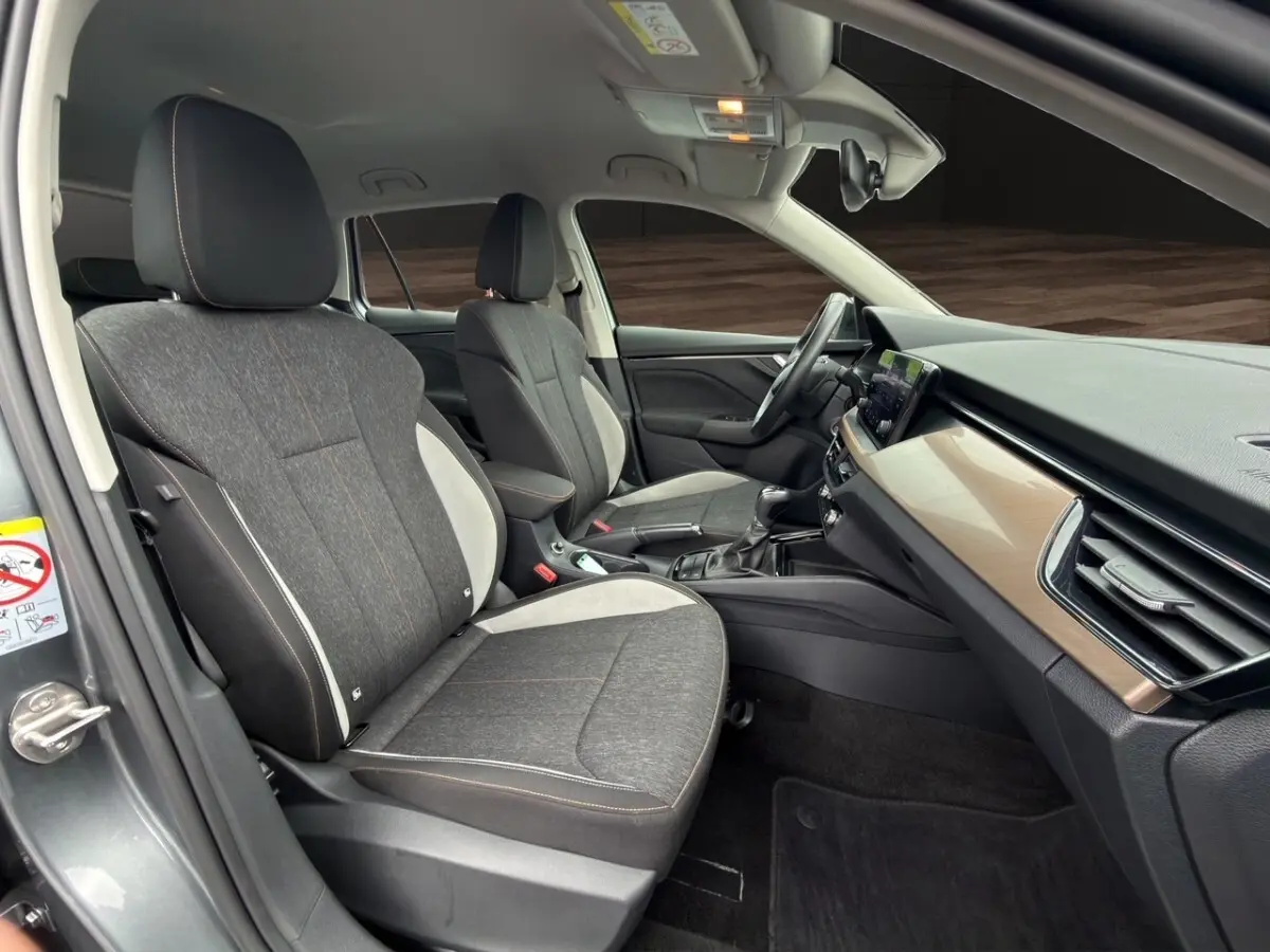 Vue intérieure côté conducteur du Skoda Kamiq 2023, sièges tissu gris bicolore avec tableau de bord bois clair.
