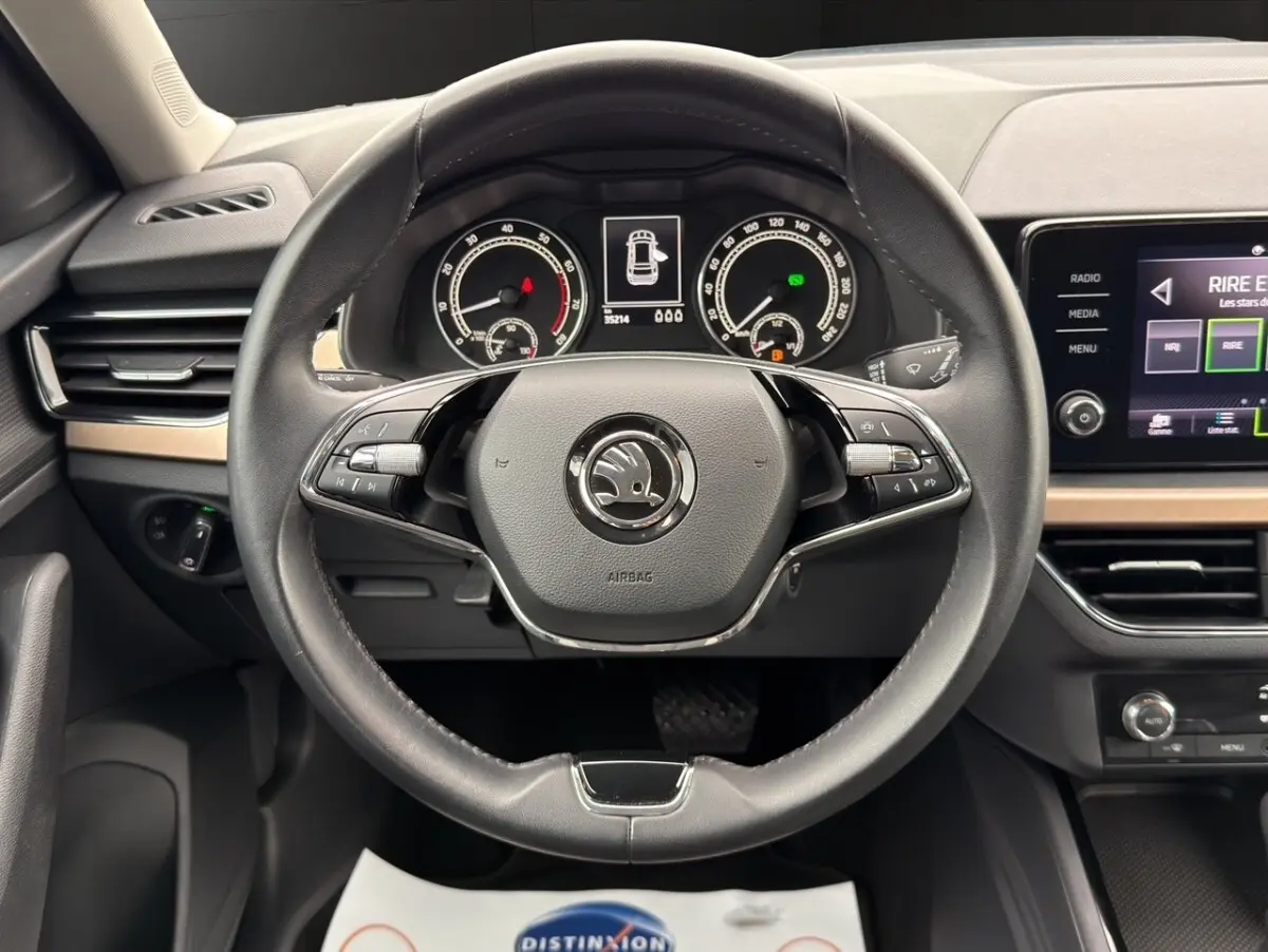 Vue centrée sur le volant cuir noir et le tableau de bord numérique du Skoda Kamiq 1.5 TSI 2023, avec écran tactile latéral.