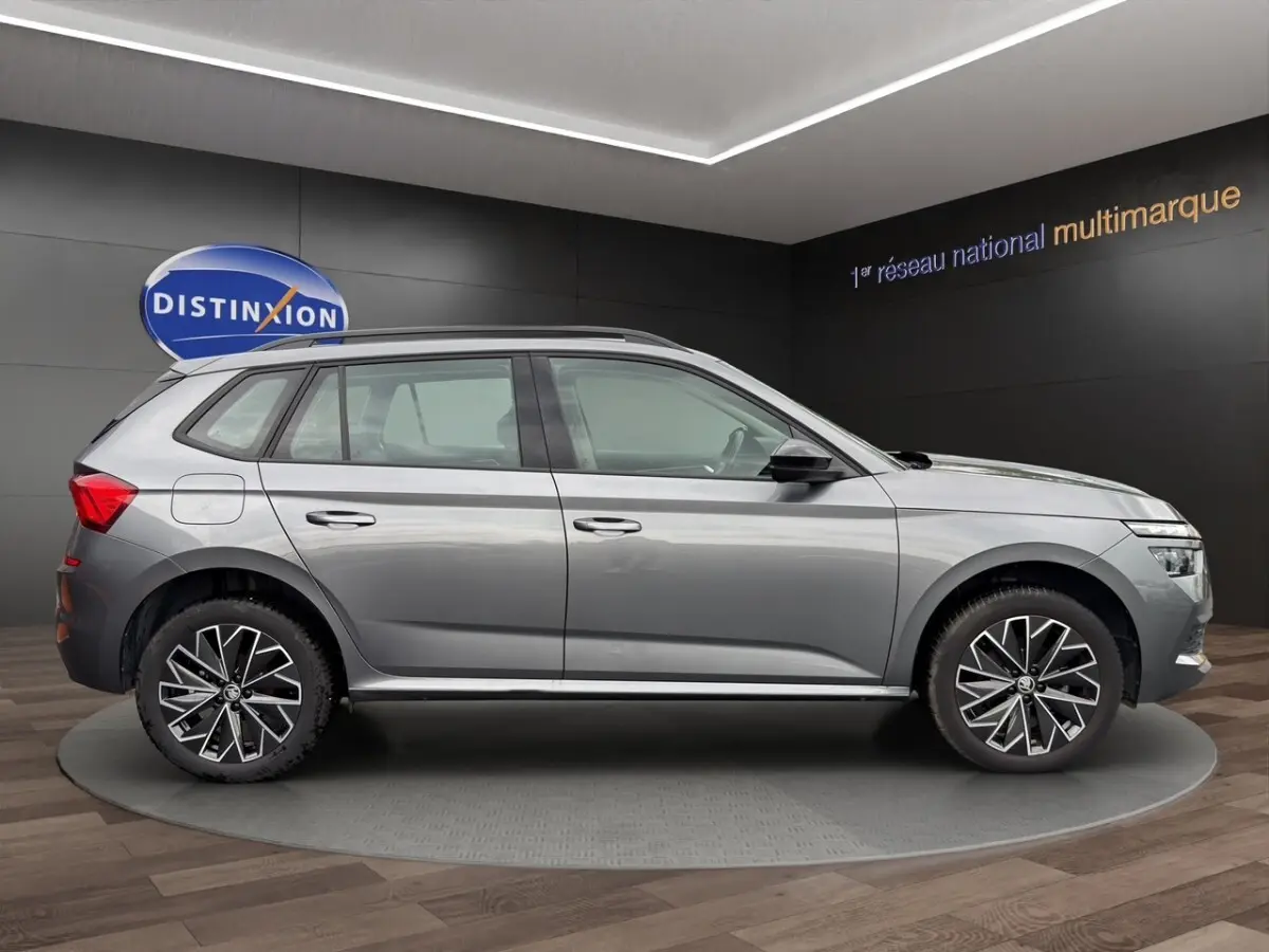 Vue de profil côté gauche du Skoda Kamiq gris foncé 2023 avec jantes bi-ton et barres de toit noires.