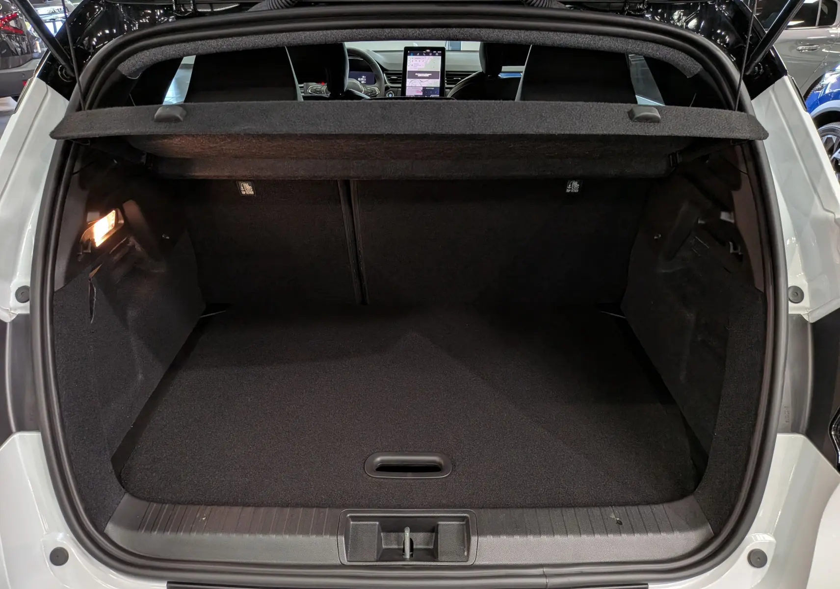 Coffre ouvert vu de l'arrière d'un Renault Captur blanc nacré avec toit noir, intérieur noir et tablette tactile visible.