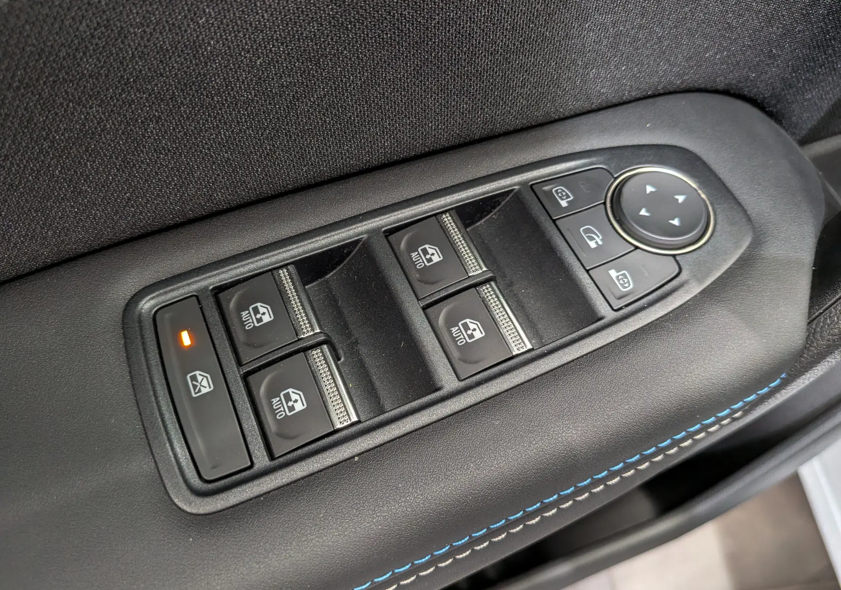 Gros plan sur les commandes des vitres et rétroviseurs côté conducteur du Renault Captur E-TECH blanc nacré, avec surpiqûres bleues.