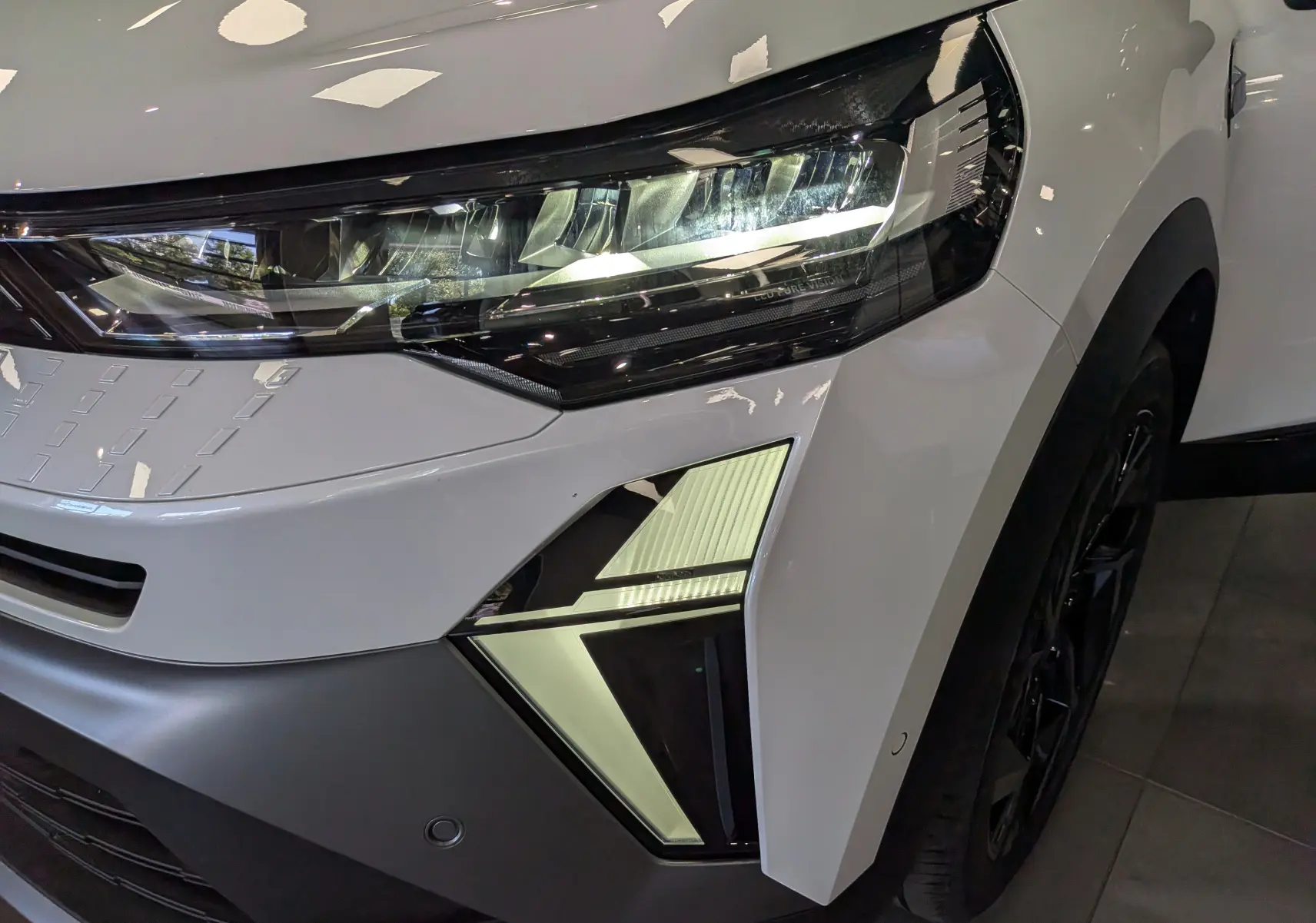 Gros plan sur l'avant droit du Renault Captur blanc nacré, mettant en valeur le phare LED et la calandre noire.