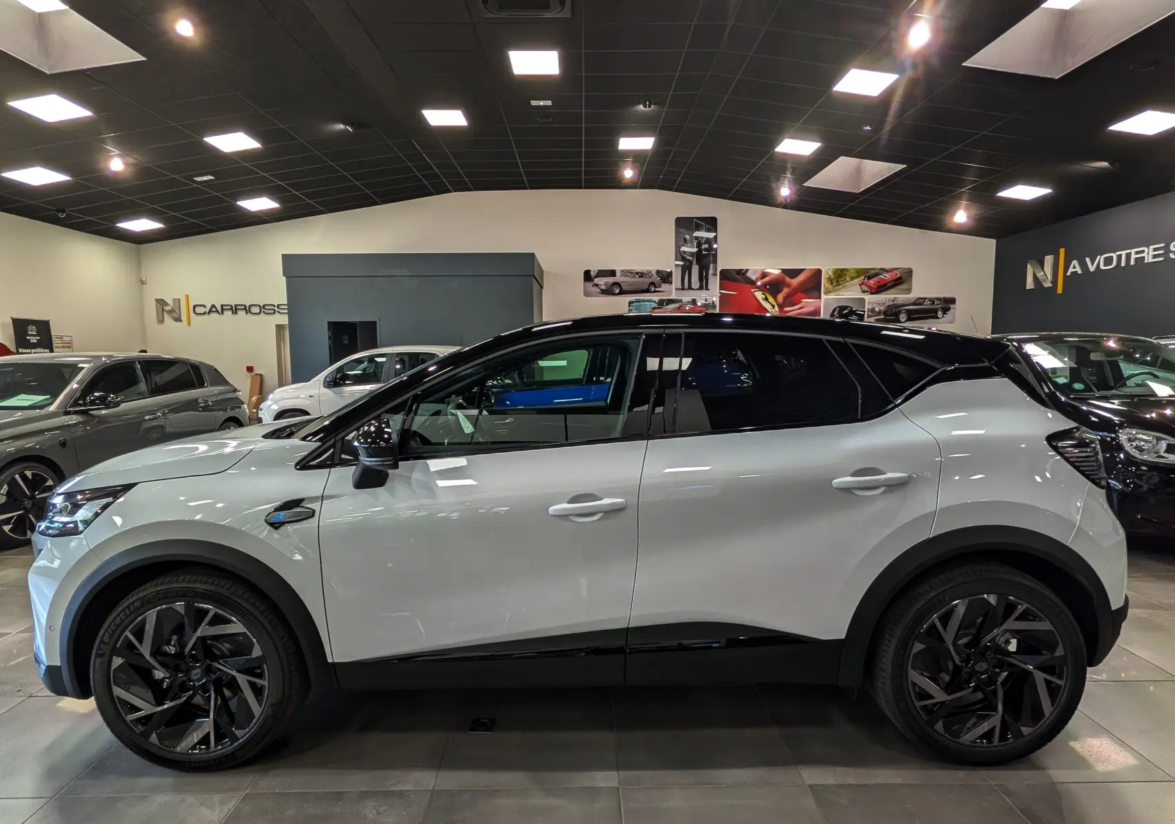 Profil côté gauche du Renault Captur E-TECH 160 ch blanc nacré avec toit noir et jantes noires en concession.