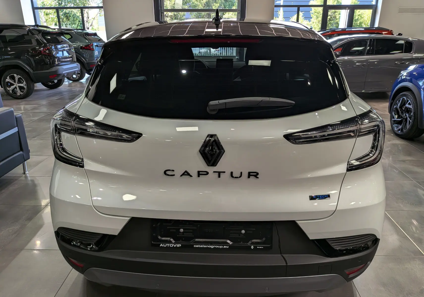 Vue arrière d'un Renault Captur E-TECH blanc nacré avec toit noir, en intérieur de showroom lumineux.