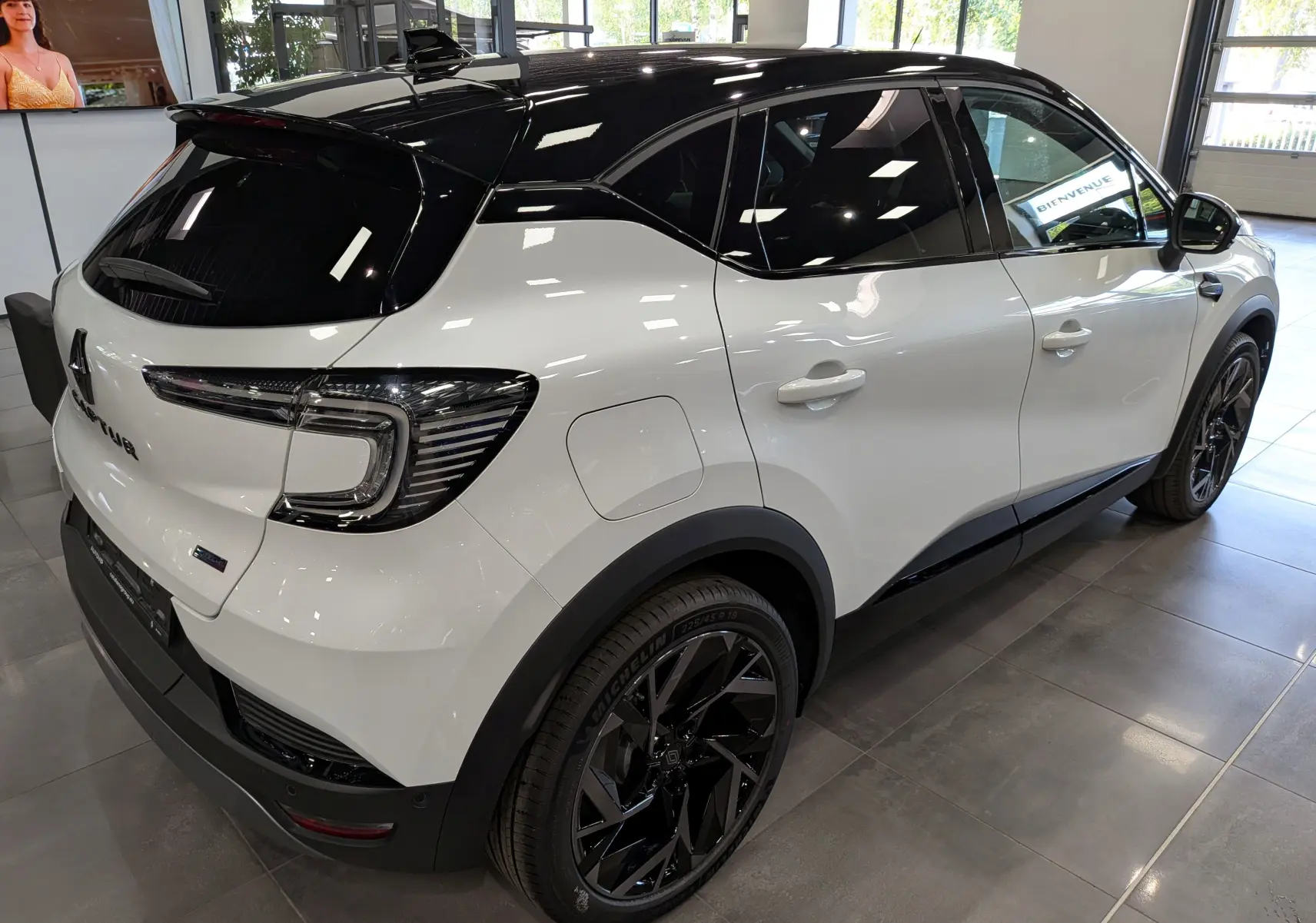Vue 3/4 arrière droite du Renault Captur E-TECH blanc nacré avec toit noir et jantes noires en showroom.