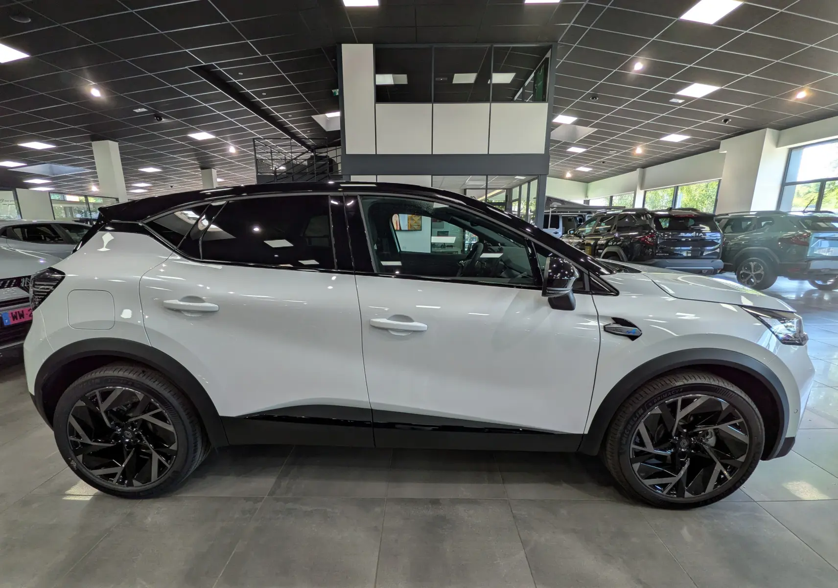 Profil côté gauche du Renault Captur E-TECH blanc nacré avec toit noir, roues noires et détails sportifs en showroom.