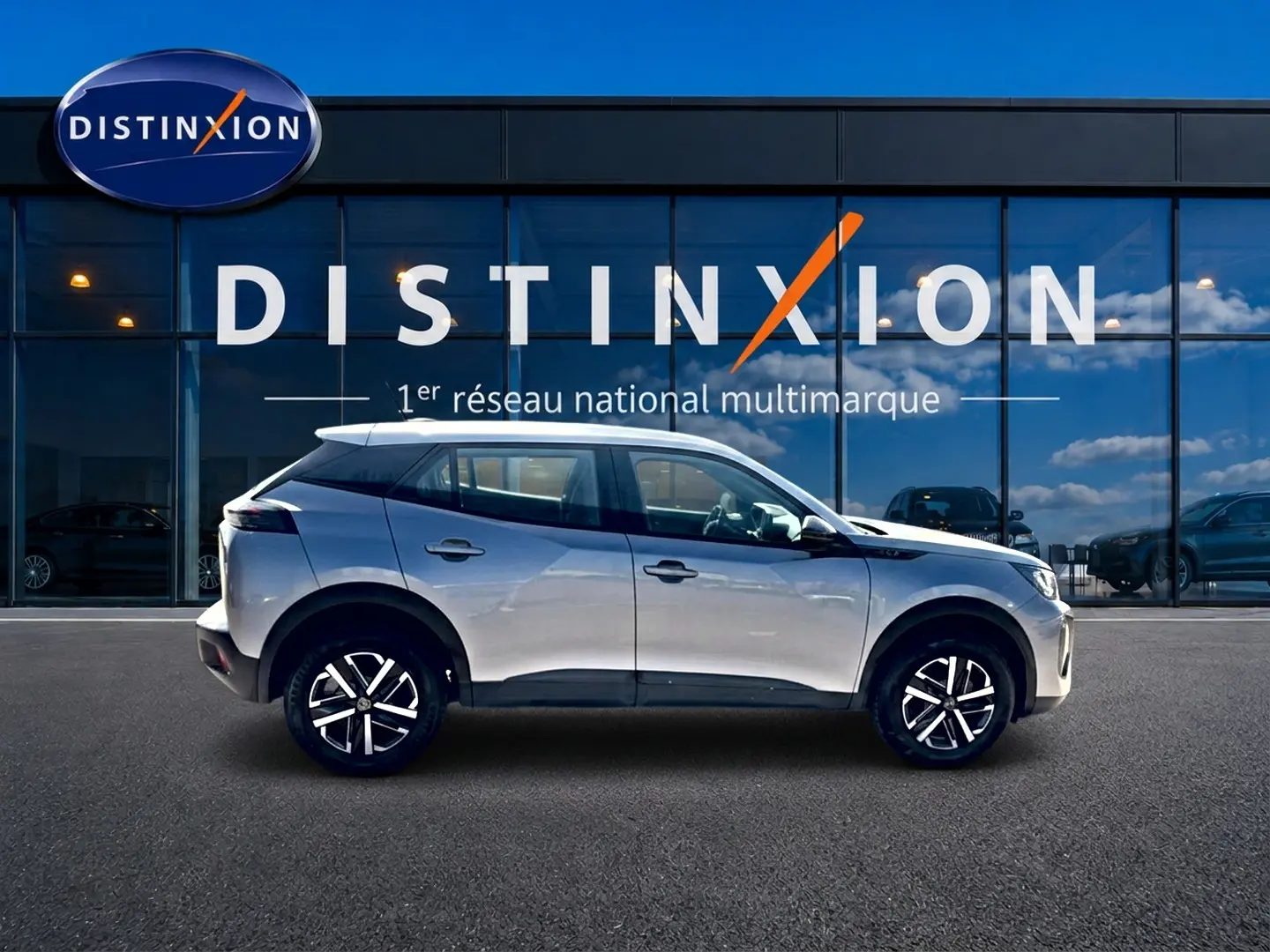 Peugeot 2008 gris en profil droit, avec jantes noires et toit blanc devant une vitrine Distinxion.