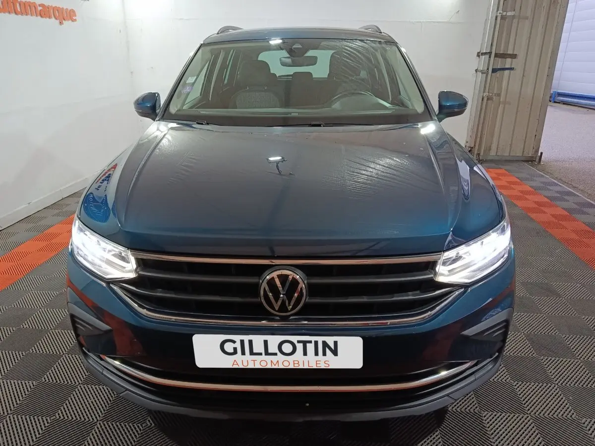 Vue avant frontale du Volkswagen Tiguan bleu avec phares LED allumés dans un showroom intérieur.