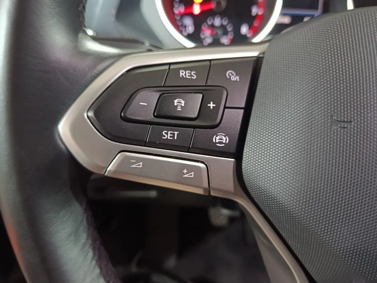 Gros plan sur le côté gauche du volant cuir du Volkswagen Tiguan bleu, avec commandes multifonctions visibles.