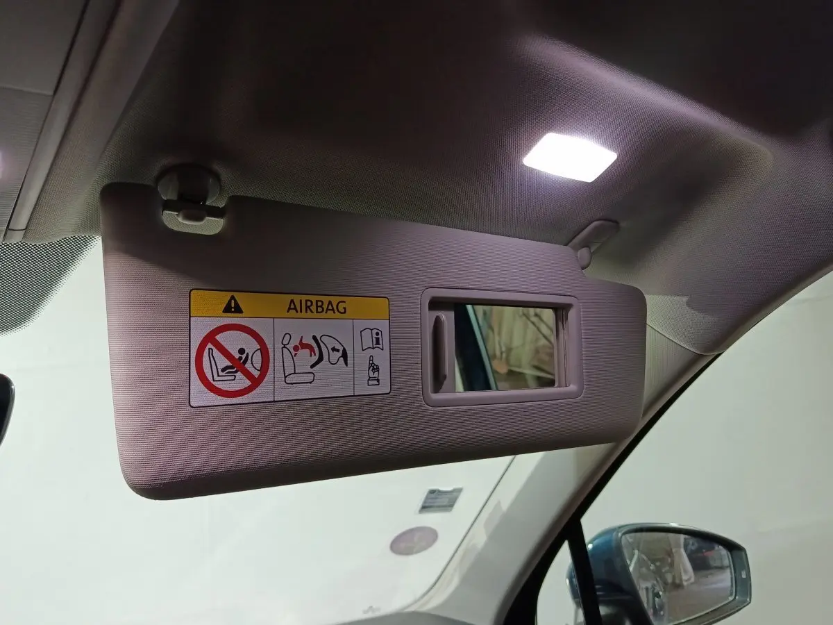 Vue intérieure sur le pare-soleil côté conducteur beige avec miroir et avertissement airbag, rétro extérieur bleu visible.