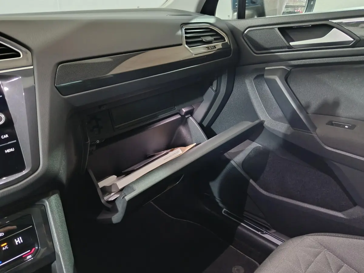 Intérieur côté passager du Volkswagen Tiguan bleu 2021, boîte à gants ouverte avec documents visibles.