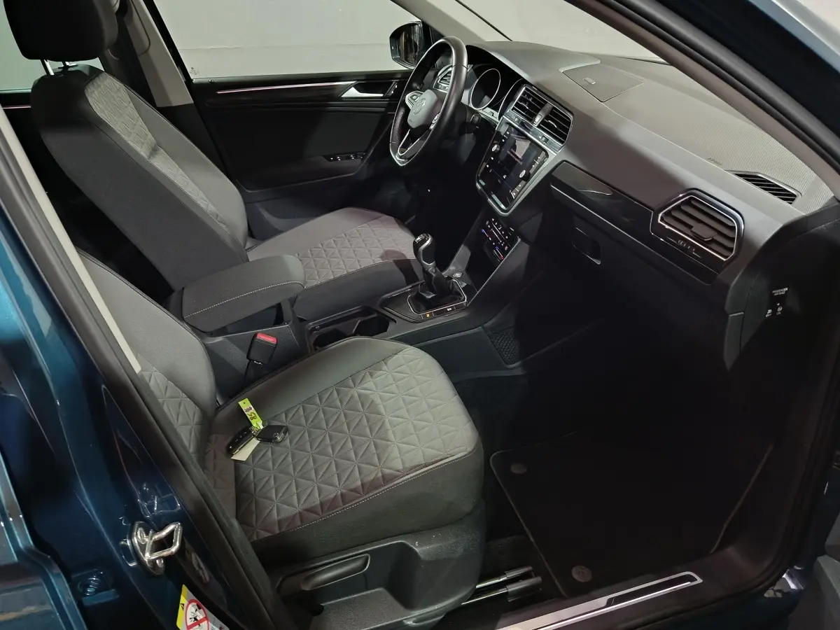 Intérieur avant droit du Volkswagen Tiguan bleu 2021, volant cuir multifonctions, sièges tissu gris à motifs géométriques.