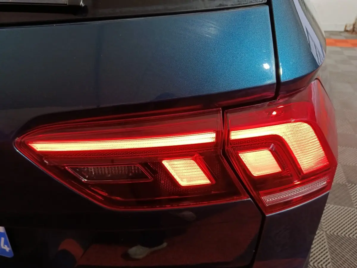 Gros plan sur le feu arrière droit allumé d’un Volkswagen Tiguan bleu métallisé, avec détails lumineux rouges et blancs.