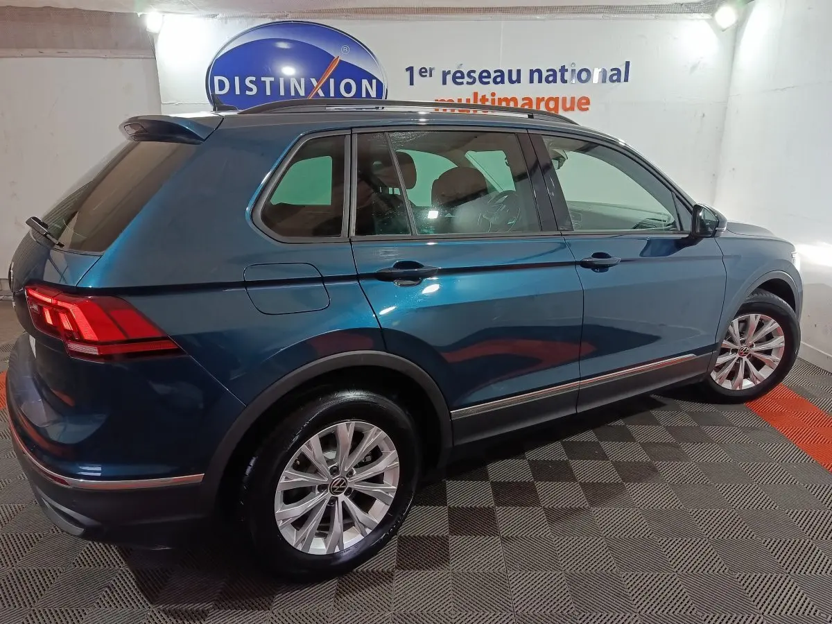Vue 3/4 arrière droite d'un Volkswagen Tiguan bleu 2021 dans un showroom avec éclairage intérieur.