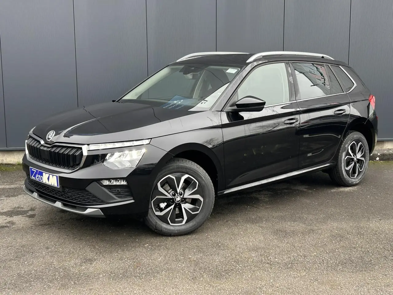 Vue 3/4 avant droite d'un Skoda Kamiq noir Magic avec jantes alliage et baguettes chromées sur fond urbain.