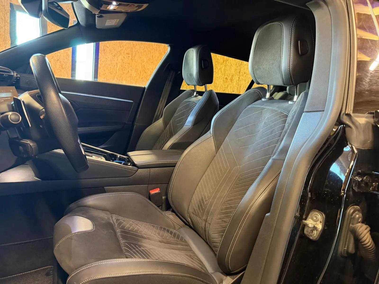 Vue intérieure côté conducteur de la Peugeot 508 SW 2024, sièges Alcantara noirs avec surpiqûres Aïkinite et volant cuir perforé.