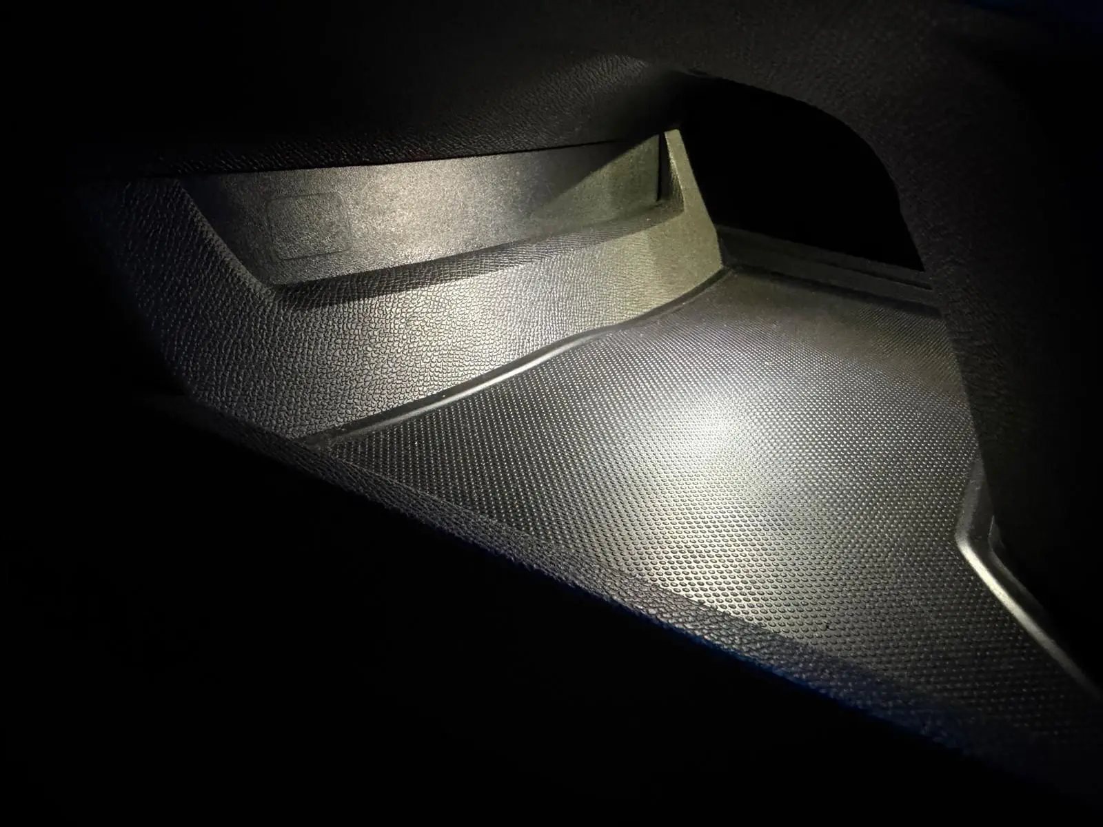 Gros plan sur le rangement intérieur noir texturé du Peugeot 508 SW 2024, éclairé par une lumière douce.