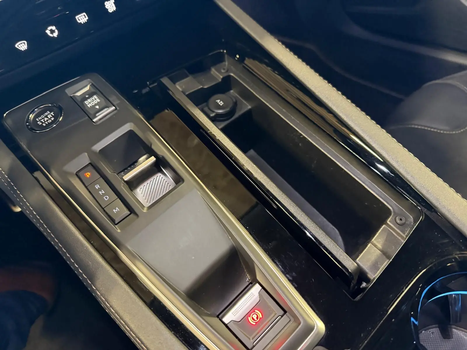 Gros plan sur la console centrale noire brillante de la Peugeot 508 SW 2024 avec sélecteur de boîte auto et frein électrique.