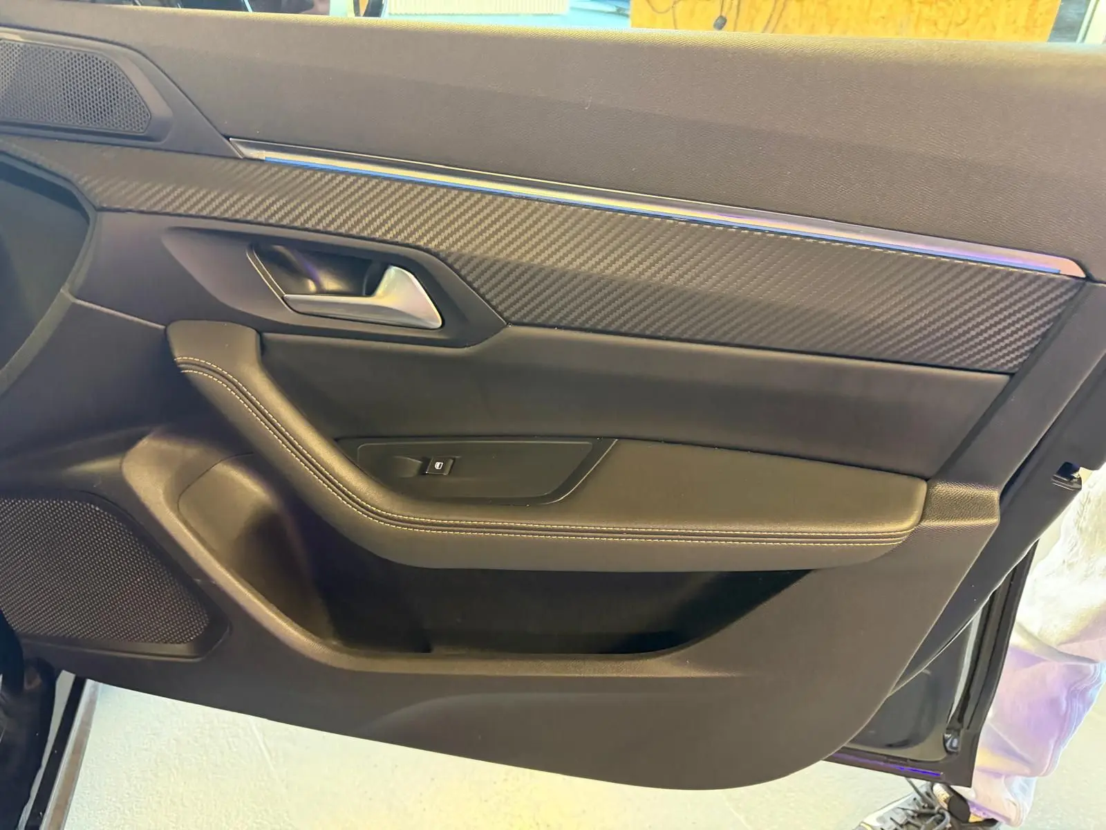 Intérieur côté gauche de porte avant noir avec insert carbone et surpiqûres blanches sur Peugeot 508 SW 2024.