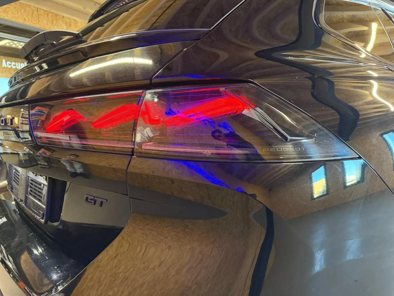 Gros plan sur le feu arrière droit rouge d’une Peugeot 508 SW GT noire brillante, avec badge GT visible.