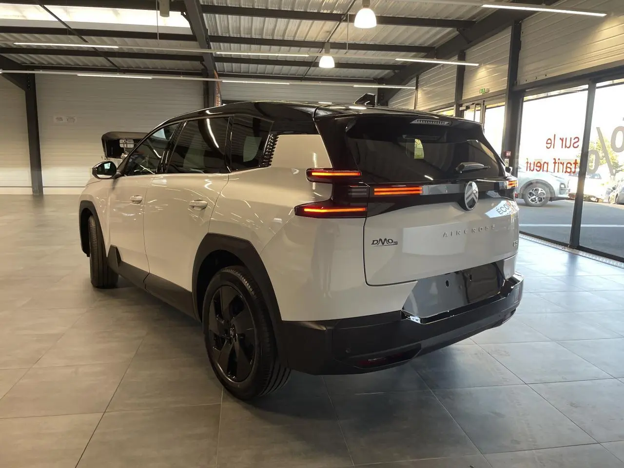 Vue 3/4 arrière droite du Citroën C5 Aircross blanc Okenite avec toit noir et feux arrière LED allumés en intérieur showroom.