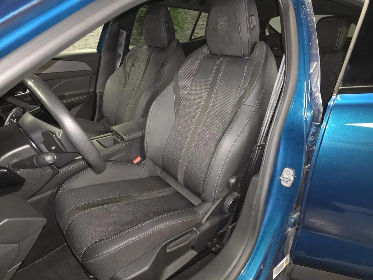 Vue intérieure côté conducteur du siège avant en tissu et cuir noir de la Peugeot 408 bleu 2024, avec appui-tête embossé Lion.
