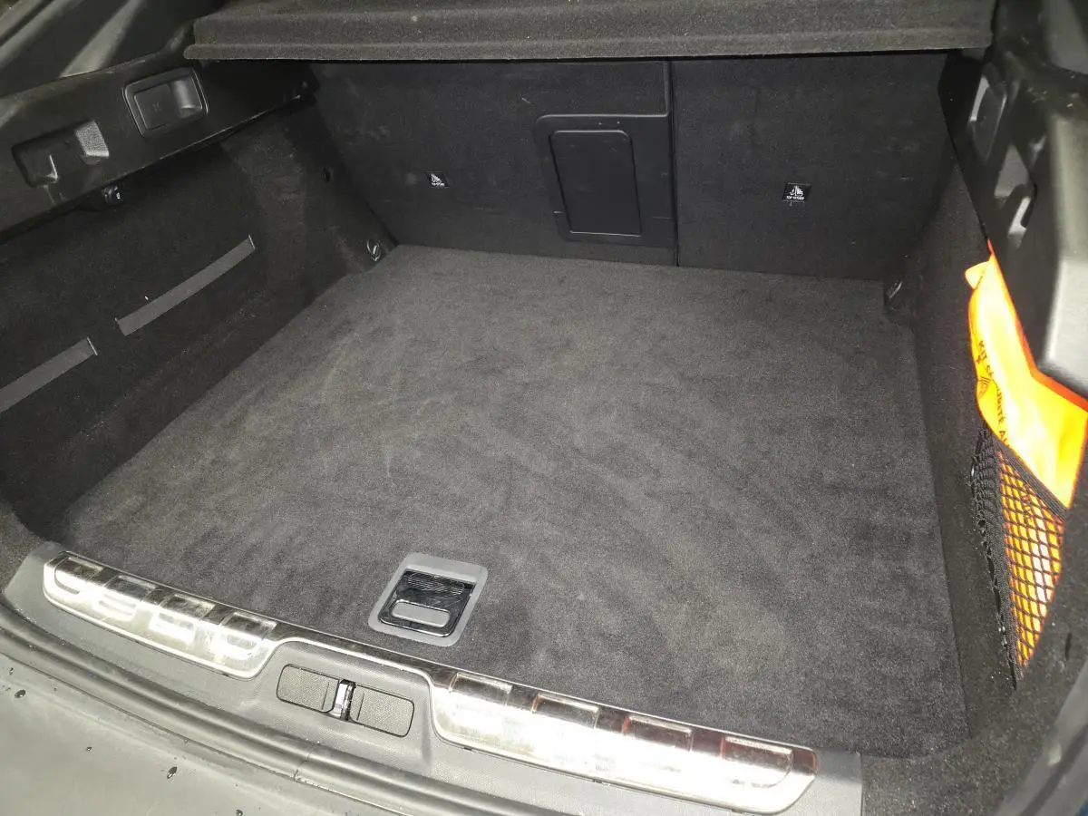 Coffre vide vu de l'arrière d'une Peugeot 408 1.6 PHEV 2024, intérieur noir avec filet de rangement latéral.