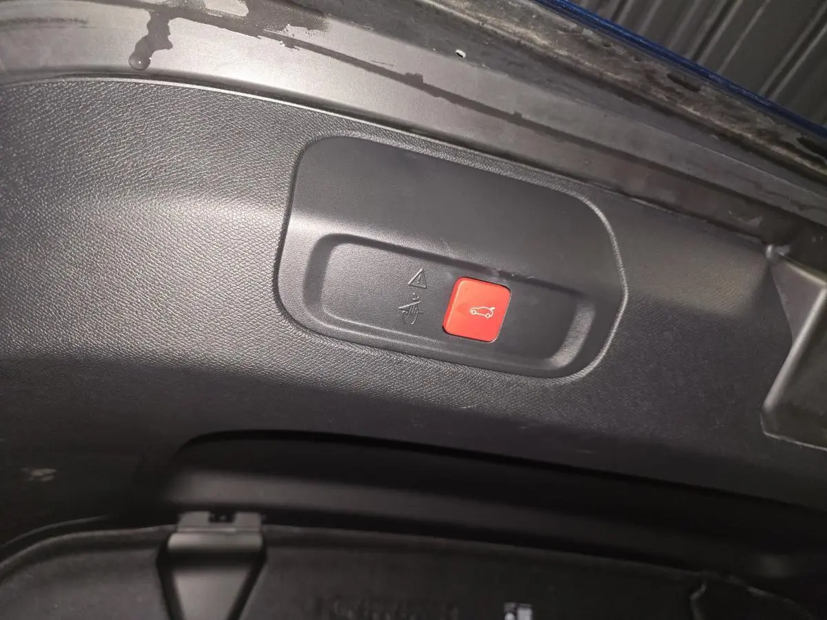 Bouton rouge d'ouverture électrique du hayon sur la partie intérieure du coffre d'une Peugeot 408 bleu.