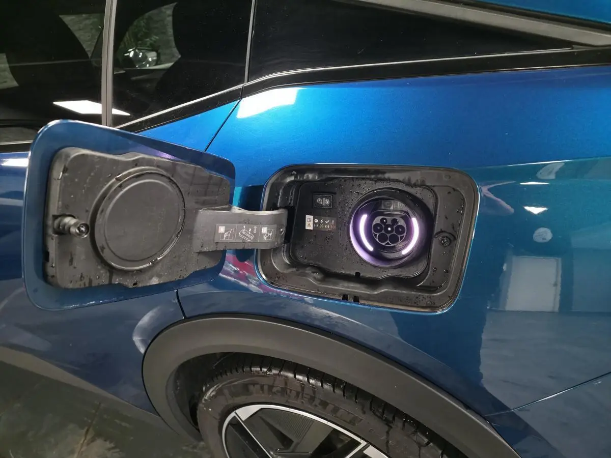 Prise de recharge ouverte côté gauche sur la carrosserie bleu métallisé du Peugeot 408 hybride rechargeable.