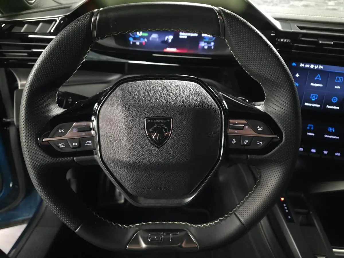 Gros plan sur le volant cuir perforé noir avec logo Peugeot et commandes intégrées du Peugeot 408 GT 2024.